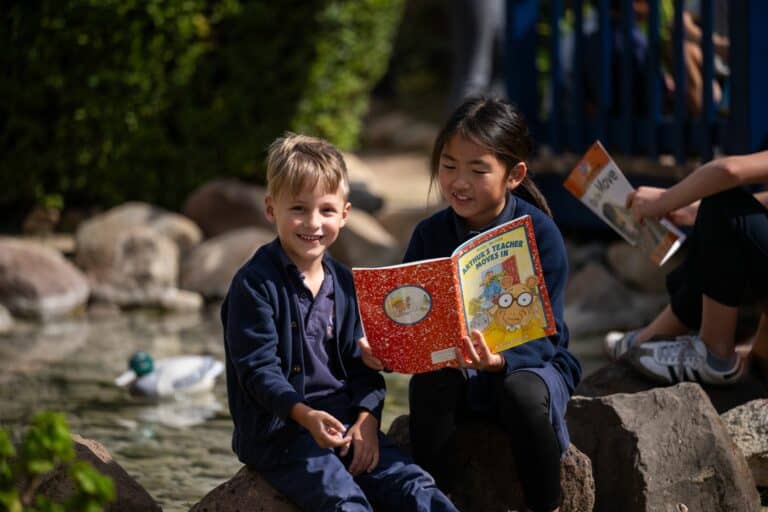Two students reading a book outdoors near a creek at Orange County Classical Academy.